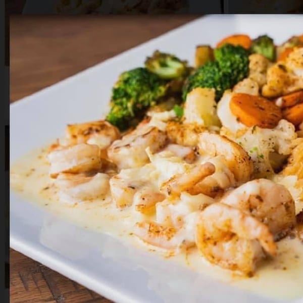 Palacio Maya's creamy shrimp dish with broccoli, carrots, and cauliflower on a white plate.