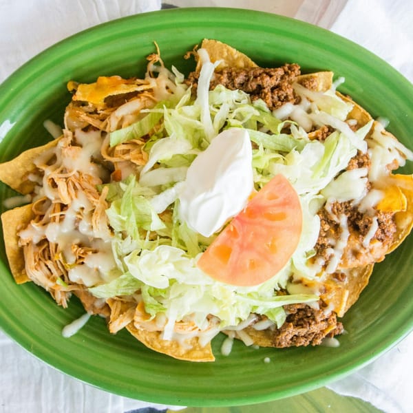 Palacio Maya's nachos with shredded chicken, ground beef, lettuce, sour cream, and tomato on a green plate.