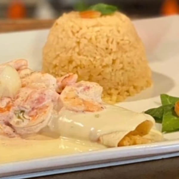 Shrimp dish with creamy sauce, rice, and a side of greens on a white plate.